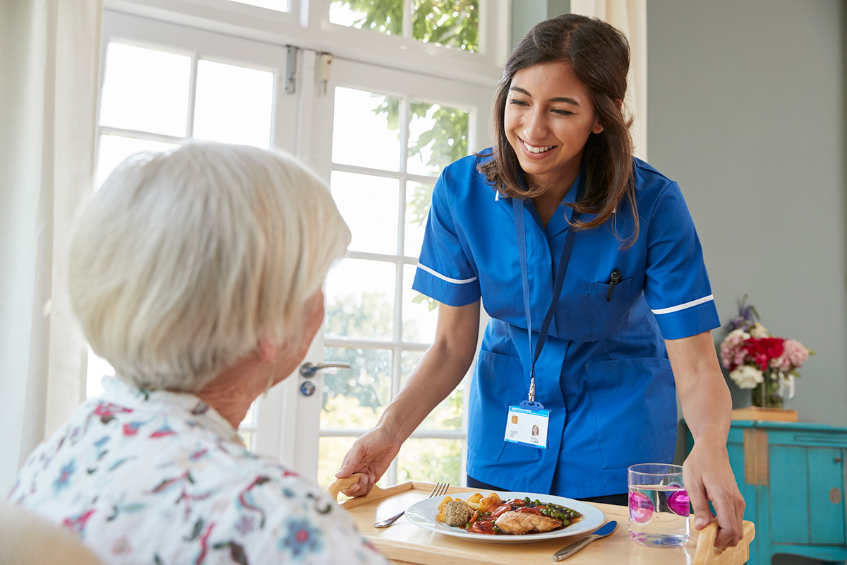 Meal Preparation Care Nurse Serving Dinner To A Senior Woman At Home