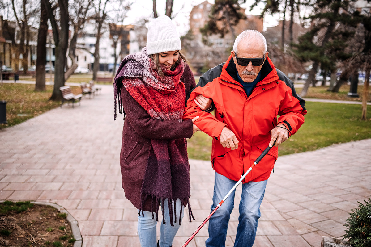 Young Female Adult Spending Time With Blind Old Person Outdoors On Winter Day And Walking Together